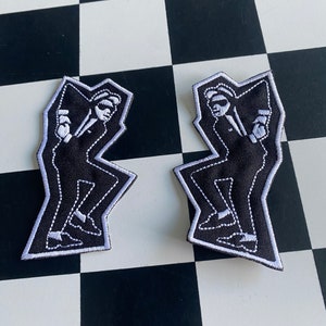 May include: Two black and white embroidered patches featuring a silhouette of a person in a suit dancing. The patches have a white outline and are on a black and white checkered background.