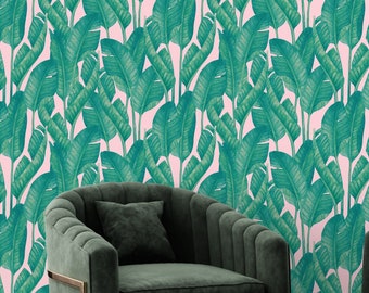 May include: Two dark green velvet armchairs with gold metal frames sit in front of a pink and green wallpaper with a tropical leaf pattern.