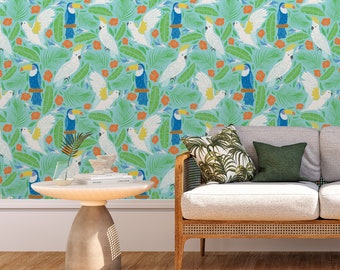 Puede incluir: Un papel tapiz tropical azul claro y verde con tucanes y cacatúas. Un sofá blanco con un cojín estampado verde y marrón y un cojín verde sólido se encuentra frente al papel tapiz. Una pequeña mesa redonda con un libro encima se encuentra frente al sofá.
