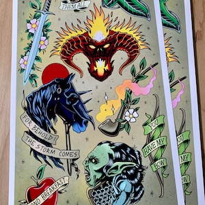 May include: A colorful tattoo flash sheet featuring various images from the Lord of the Rings, including the One Ring, the Eye of Sauron, a pipe, a sword, an apple, and a goblin. The text on the sheet includes "To Rule Them All", "For Behold! The Storm Comes", "Second Breakfast", and "You Have My Bow".