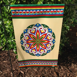 Könnte beinhalten: Eine beige Gartenflagge mit einem farbenfrohen Mandala-Design in der Mitte. Das Mandala zeigt die Farben Rot, Gelb, Grün, Blau und Weiß. Die Flagge hat einen grünen, roten, gelben und blauen Rand.