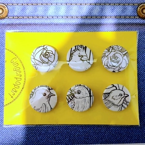 May include: A set of six black and white illustrated buttons featuring a bird, a rose, and a parrot. The buttons are packaged on a yellow card with the text "Gingerpoppet".