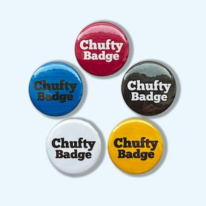 Puede incluir: Un conjunto de cinco botones redondos en varios colores: rojo, azul, negro, blanco y amarillo. Cada botón presenta el texto "Chuffy Badge" en blanco y negrita. Los botones están dispuestos en un patrón circular sobre un fondo azul claro.