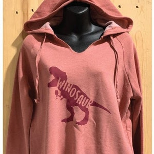 May include: A pink hooded sweatshirt with a burgundy dinosaur graphic and the text "Winosaur" printed on the front.