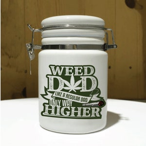 May include: A white ceramic jar with a hinged lid and metal clasp. The jar features the text "WEED DAD" with a cannabis leaf graphic, and the phrase "LIKE A REGULAR DAD ONLY WAY HIGHER" in green.