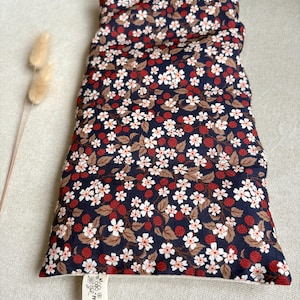 Könnte beinhalten: Ein rechteckiges Kissen mit einem floralen Muster auf marineblauem Hintergrund. Es zeigt weiße Blüten, rote Beeren und braune Blätter. Das Kissen ist gefüllt und hat ein weiches Aussehen. Ein kleines Etikett ist angebracht.