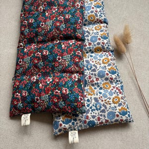 Könnte beinhalten: Drei rechteckige Kissen mit Blumenmustern. Eines hat einen dunkelblauen Hintergrund mit roten und blauen Blumen. Ein anderes hat einen weißen Hintergrund mit blauen und gelben Blumen. Das dritte Kissen hat ein ähnliches Blumenmuster wie das erste.