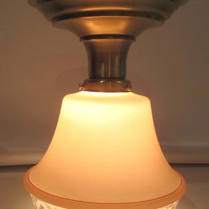 May include: A vintage ceiling light fixture with a brass finish. The light has a bell-shaped, frosted glass shade with a floral pattern around the bottom edge. The fixture is designed to be mounted on the ceiling.