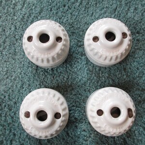 May include: Four white ceramic light fixture canopies with a central hole and two smaller holes. The canopies have a ridged design around the edge and are arranged on a teal-colored surface.