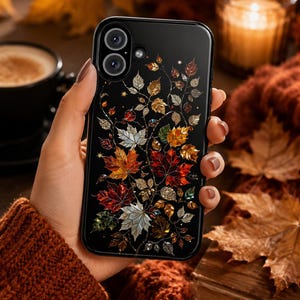 May include: A black smartphone case featuring a detailed design of autumn leaves in shades of red, orange, gold, and silver. The leaves are arranged in a branching pattern across the back of the case, accented with small sparkling star shapes.