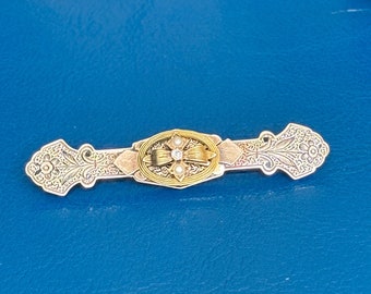 May include: An antique brooch with an oval center featuring a diamond and small pearls, surrounded by gold filigree. The brooch has a silver-toned base with ornate floral and scrollwork designs.