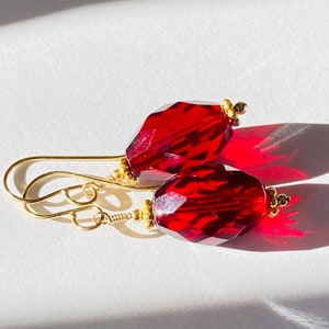 May include: A pair of red gemstone earrings with gold accents. The earrings are dangle style with a teardrop shaped gemstone.