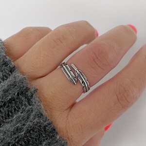 May include: A silver ring featuring two feather designs. The ring is adjustable and can be worn on any finger.