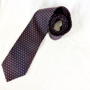 May include: A dark navy blue necktie featuring a repeating geometric pattern of thin, diagonal red lines intersected by small, horizontal gold-colored dashes. The tie is coiled at the top and extends downward, displaying a pointed end at the bottom.