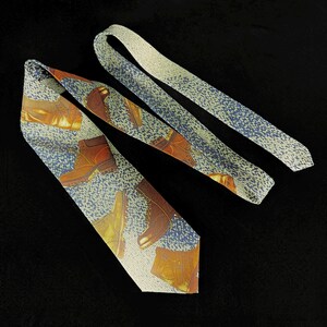 May include: A necktie featuring a repeating pattern of brown leather work boots set against a textured background of blue and white speckled fabric. The tie displays multiple boot orientations and a pointed tip, showcasing a detailed graphic print.
