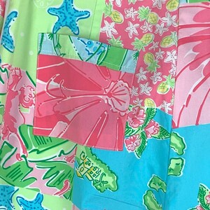 Pu&ograve; includere: Un tessuto patchwork con una variet&agrave; di motivi colorati, tra cui fiori rosa, foglie verdi, stelle marine blu e ananas gialli. Il tessuto ha una tasca blu chiaro con un motivo di fiori rosa.