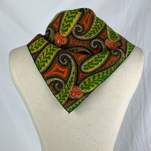 Peut inclure: Un bandana &agrave; motif paisley vert, orange et marron. Le bandana est pli&eacute; en forme de triangle et est pr&eacute;sent&eacute; sur un mannequin blanc.