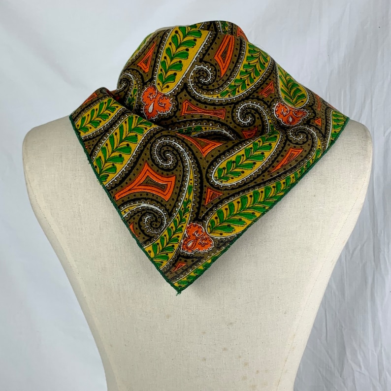 Peut inclure: Un bandana &agrave; motif paisley vert, orange et marron. Le bandana est pli&eacute; en forme de triangle et est pr&eacute;sent&eacute; sur un mannequin blanc.