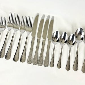 May include: A set of stainless steel silverware, including forks, knives, and spoons. The handles have a textured, hammered design. The silverware is arranged on a white surface.