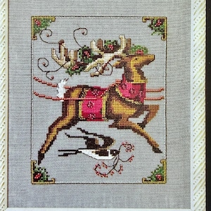 May include: Cross-stitch design of a reindeer in a running pose, adorned with a festive harness and antlers decorated with holly. The reindeer is set against a gray background, framed with decorative corners.