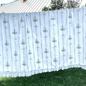 May include: White cotton curtain panel with a green floral print and a white lace trim. The curtain is hanging on a clothesline.
