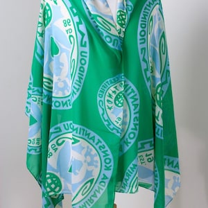 May include: A green chiffon scarf with a repeating pattern of blue and white circles. The circles contain the text "KONS TITVATSI KONOK AD 1938" and other text in a foreign language.
