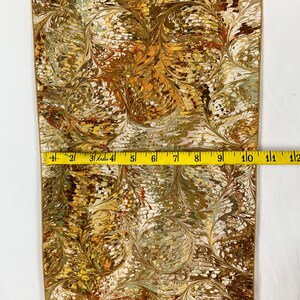 Peut inclure: Un tissu marbr&eacute; or et brun sur fond blanc. Le tissu est mesur&eacute; avec un ruban &agrave; mesurer, montrant qu'il mesure 12 pouces de large.