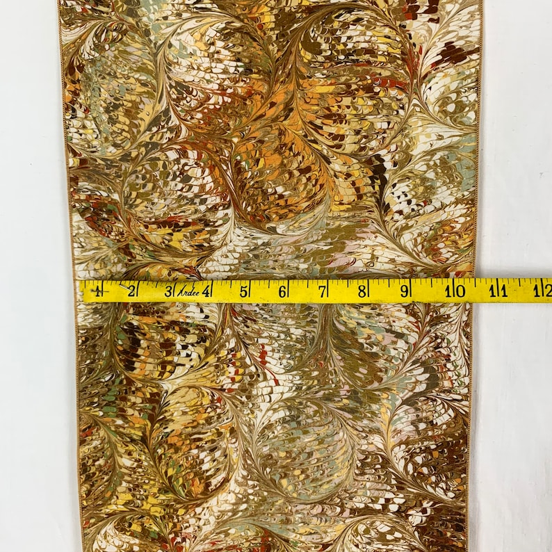 Peut inclure: Un tissu marbr&eacute; or et brun sur fond blanc. Le tissu est mesur&eacute; avec un ruban &agrave; mesurer, montrant qu'il mesure 12 pouces de large.