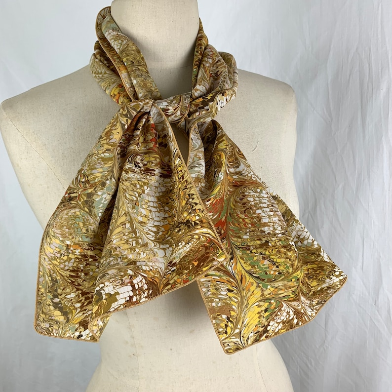 Peut inclure: Un foulard en soie marron et or avec un motif marbr&eacute;. Le foulard est nou&eacute; autour du cou d'un mannequin.