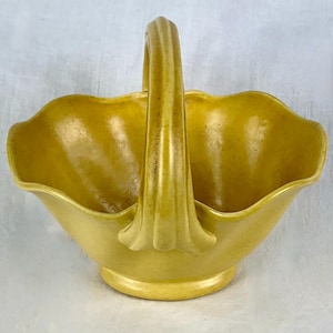 May include: A yellow ceramic basket with a scalloped rim and a handle. The basket is made in a classic style and would be perfect for holding small items.