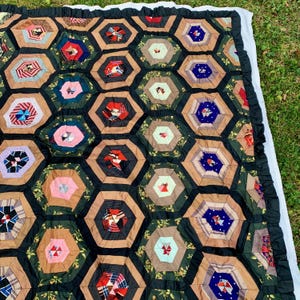 May include: A patchwork quilt with a hexagonal pattern. The quilt is made of various fabrics in shades of brown, green, pink, blue, and red. The quilt is edged with a ruffled border.