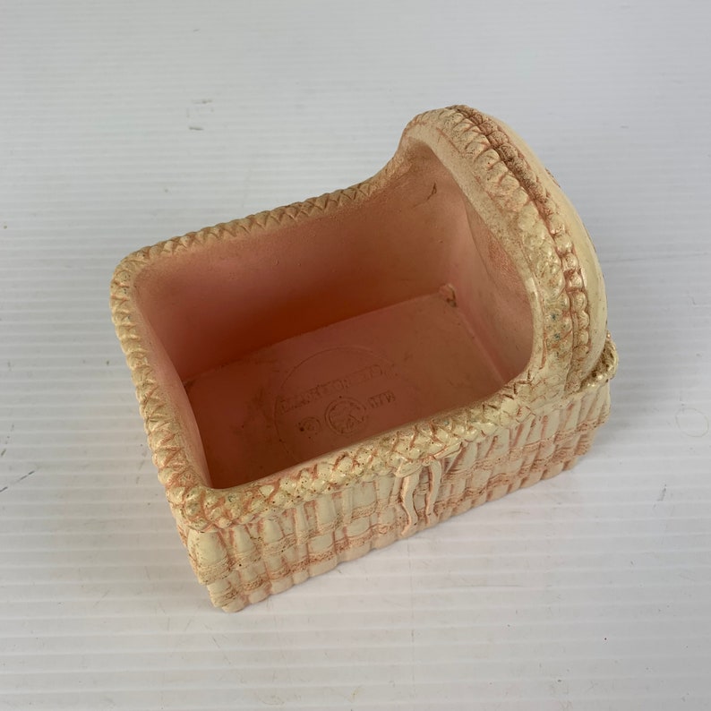 May include: A white wicker doll crib with a pink interior. The crib has a woven design and a raised headboard.