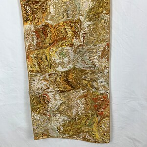 Peut inclure: Un chemin de table rectangulaire en tissu long avec un motif marbr&eacute; dans les tons de brun, or, blanc et vert. Le motif ressemble &agrave; des feuilles et des cercles tourbillonnants.