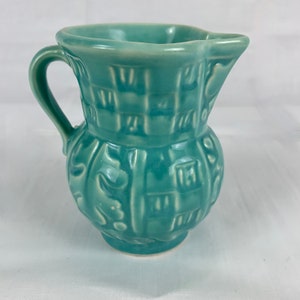 May include: A teal blue ceramic pitcher with a textured design. The pitcher has a handle and a rounded body.