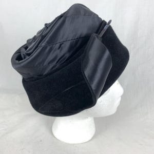 May include: A black velvet hat with a satin bow on the side. The hat is on a white mannequin head.