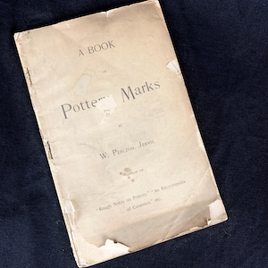 May include: A vintage book titled "A Book of Potter Marks" by W. Percival Jervis, author of "Rough Notes on Pottery" and "An Encyclopedia of Ceramics".
