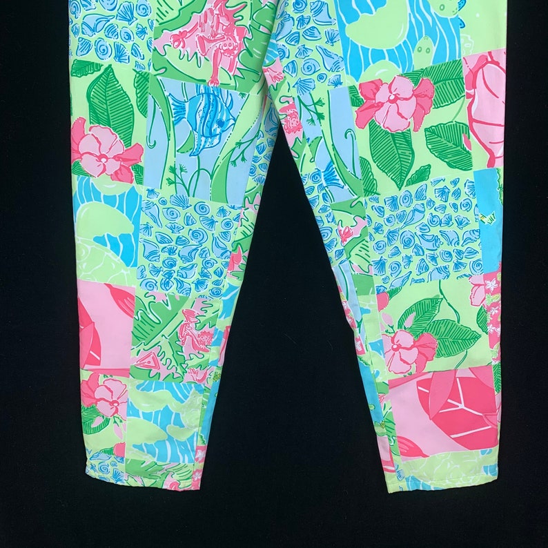 Pu&ograve; includere: Un paio di pantaloni di colore azzurro, rosa e verde con un design a patchwork che presenta conchiglie, pesci e fiori.