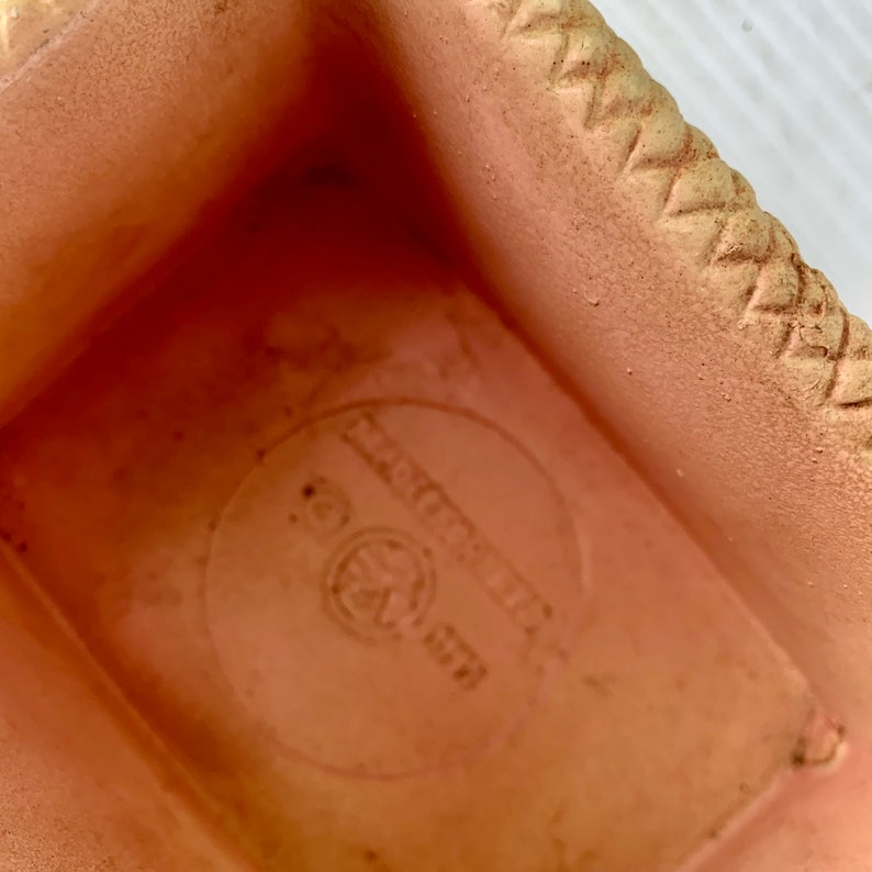 May include: A terracotta planter with a woven rim and a circular logo on the bottom that reads "Manufactured in USA".