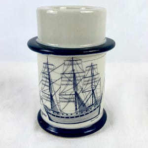 May include: A white ceramic mug with a blue band around the top and bottom. The mug features a black and white illustration of a sailing ship with the text "The " on the side.