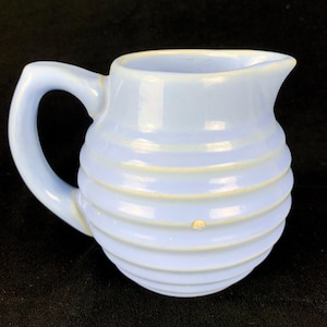 May include: A light blue ceramic creamer with a ribbed design and a handle.