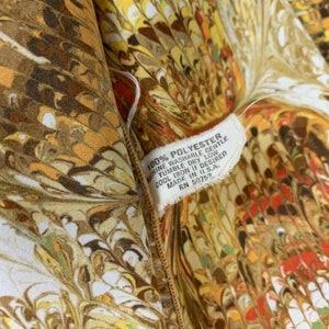 Peut inclure: Gros plan sur un tissu brun et blanc avec un motif tourbillonnant. Le tissu est muni d'une &eacute;tiquette blanche avec le texte "100% POLYESTER MACHINE WASHABLE GENTLE TUMBLE DRY LOW COOL IRON IF DESIRED MADE IN U.S.A. RN 50752".