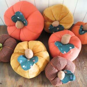 May include: A collection of six handmade fabric pumpkins in various colors and patterns. The pumpkins are made of a soft, plush fabric and have a variety of textures. They are perfect for fall decorating.