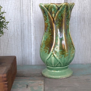May include: A green ceramic vase with a tulip shape and gold accents. The vase has a textured surface and a wide base.