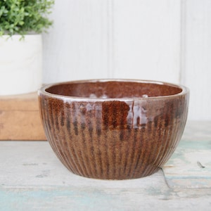 May include: A brown ceramic bowl with a textured, striped pattern. The bowl is round and has a slightly flared lip.