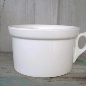 May include: A white ceramic mug with a black handle and the text "But First, Coffee" in a bold, black font. The mug is set against a neutral background, highlighting its simple design.