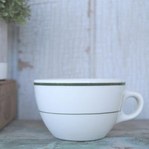 May include: A white ceramic mug with a black handle and the text "But First, Coffee" in a bold, black font. The mug is set against a blurred background, suggesting a cozy setting.