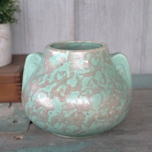 May include: A green ceramic vase with a mottled glaze and two handles. The vase has a rounded body and a wide opening.