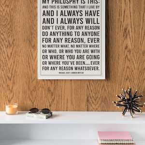 May include: A framed print with the quote "My Philosophy Is This" by Michael Scott from The Office. The print is displayed on a white shelf with sunglasses, a candle, and a decorative object.