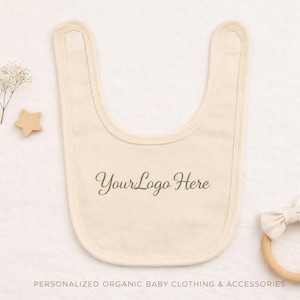 May include: Cream-colored baby bib with the text "YourLogo Here" in a script font. A wooden star and a wooden teething ring with a bow are also present. The image also includes the text "PERSONALIZED ORGANIC BABY CLOTHING & ACCESSORIES".