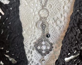May include: A silver-toned pendant necklace featuring an ornate, filigree-style centerpiece adorned with four white faux pearls. The pendant includes a crescent moon charm with clear crystals, a dark bead, and a clear teardrop-shaped crystal.